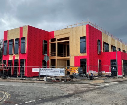 A photo of showing the progress of construction of a new office, family centre, and library at Union Street, Ellon. The photo shows the two-storey wooden frame of the building, with most of the windows installed. The site is bounded on two sides by roads, and protective metal fencing surrounds the site. Some construction equipment is within the site.  