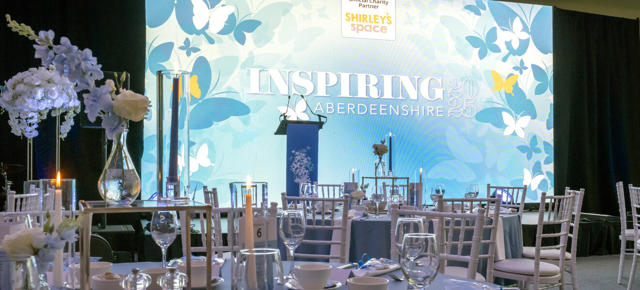Inspiring Aberdeenshire banner on a presentation screen, with tables and glasses in the foreground