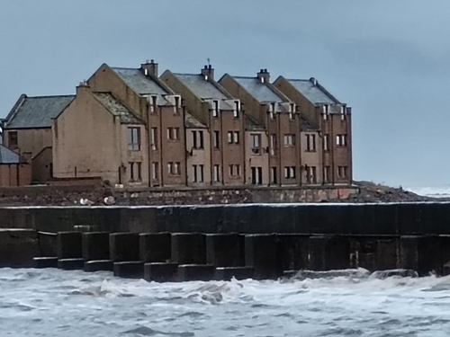 View of property from the other side of the harbour. A row of properties lie near the sea.
