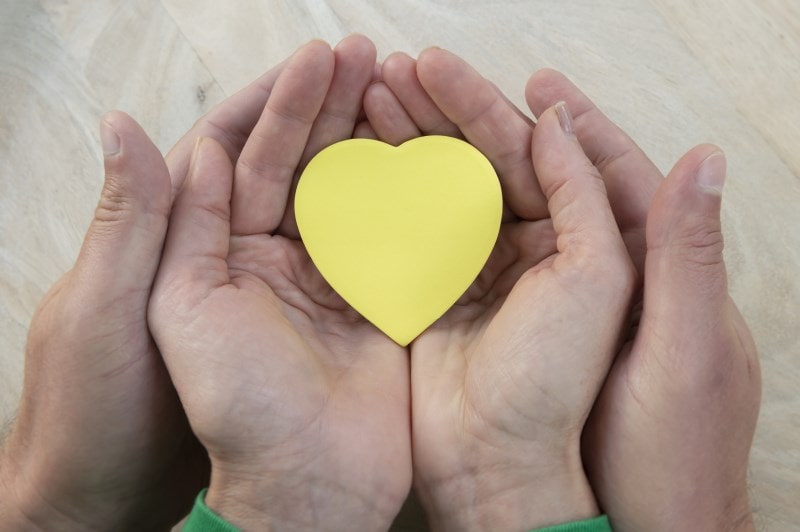 Pair of hands holding a yellow paper heart