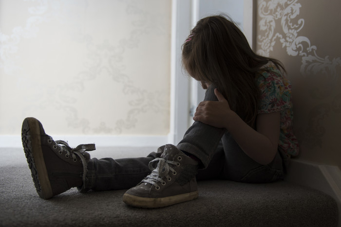 Vulnerable young girl sitting on stairs in a dark corridor