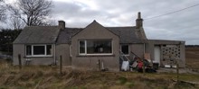 A house surrounded by land with large windows and a barbed wire fence