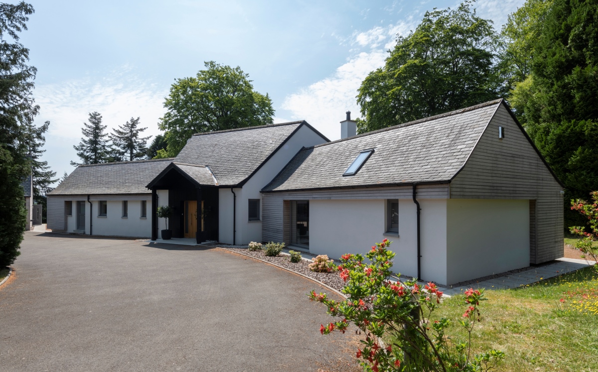 Bungalow house with extension, driveway and trees in the background