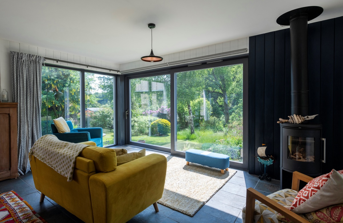 Inside view of Burnside cottage showing wood burner, various furniture and sofa facing glass wall