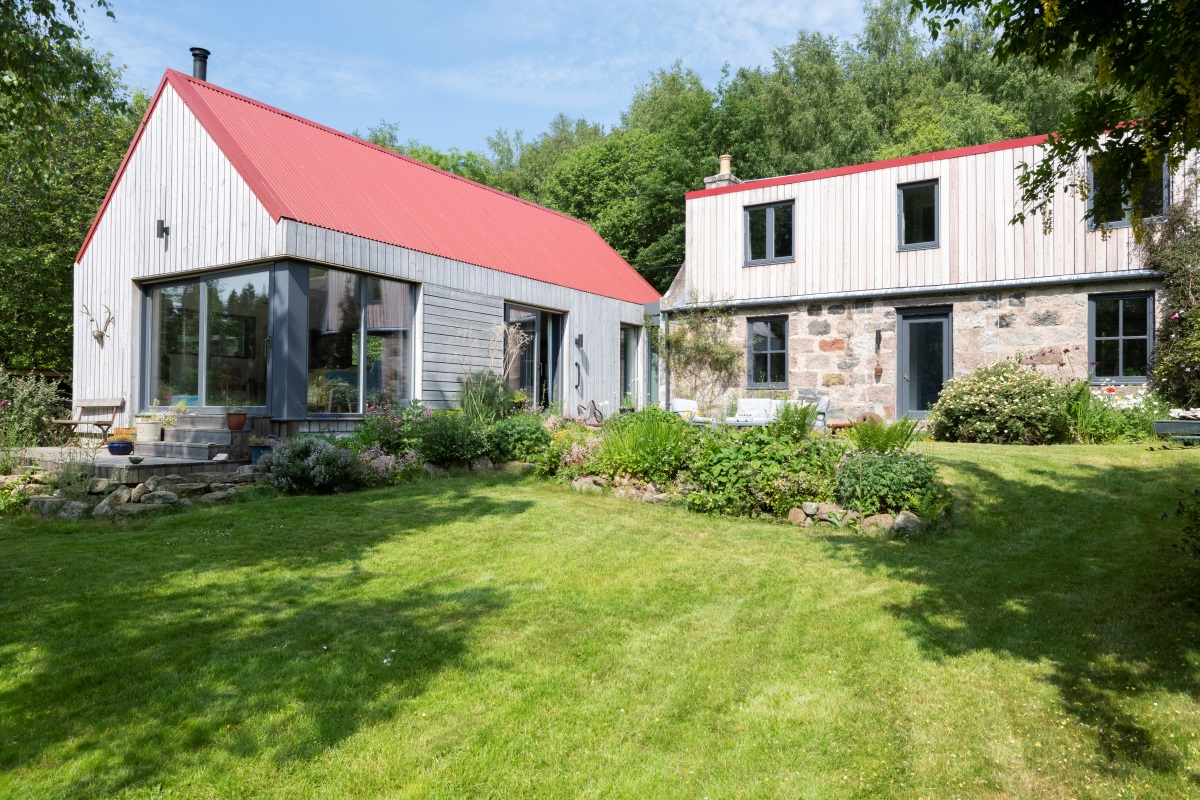 Cottage with cladding, large window screens and grass area in foreground