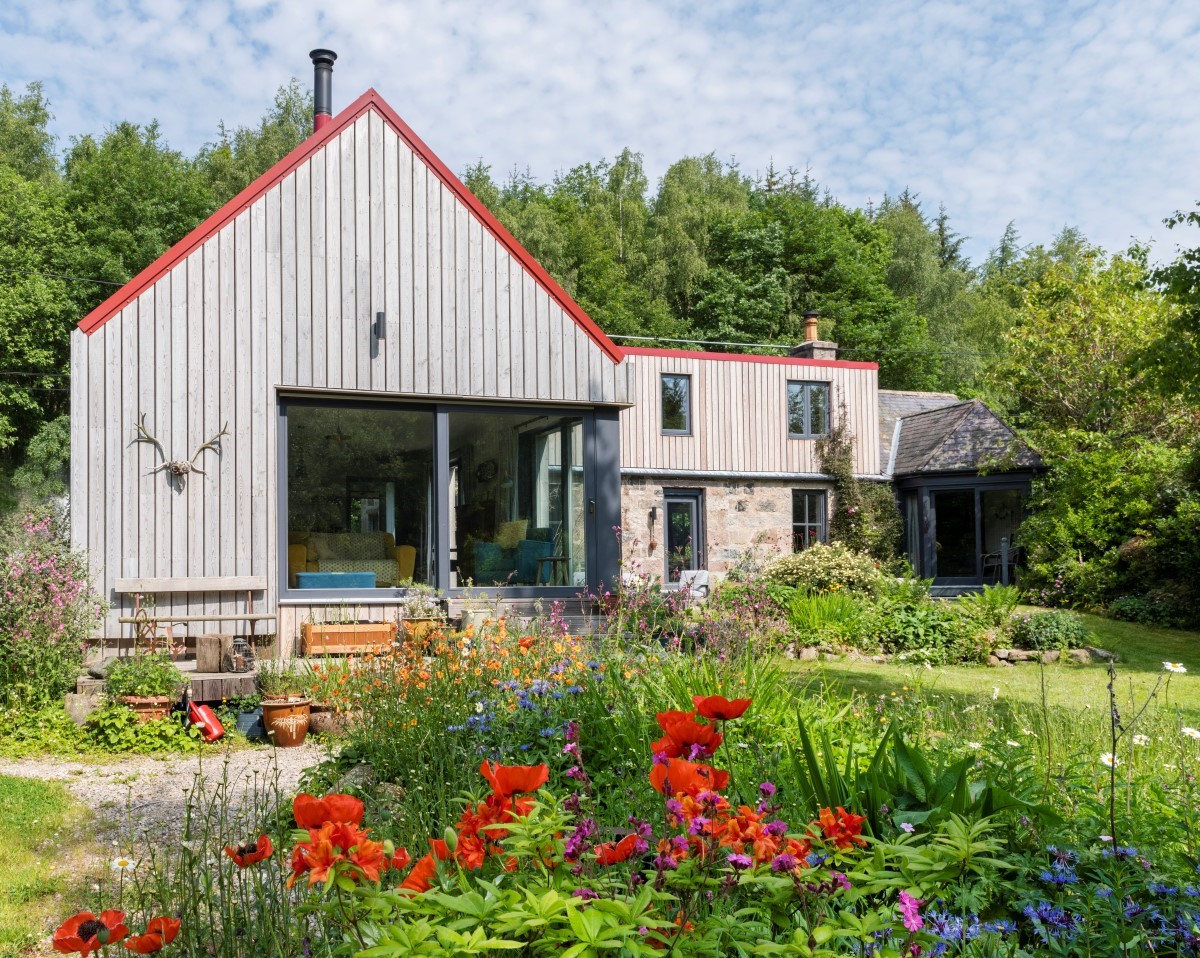 Cottage with Scottish Larch cladding, large window screens and flowers in the foreground