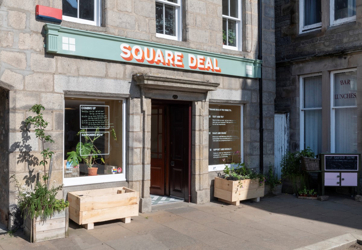 Building with large sign that reads Square Deal and two large windows with writing on them