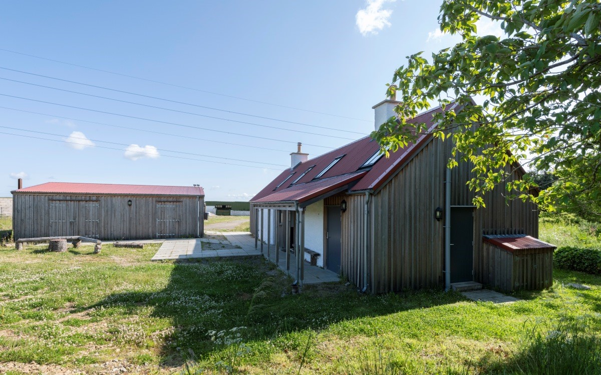 Renovated farm house with cladding, shed building in the background and large grass area