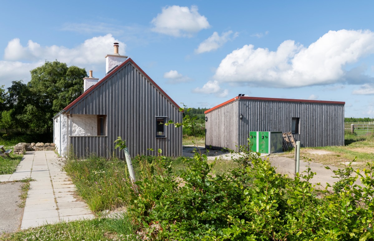 Side view of Greenmyres farm building with cladding and shed with cladding, with plants in foreground