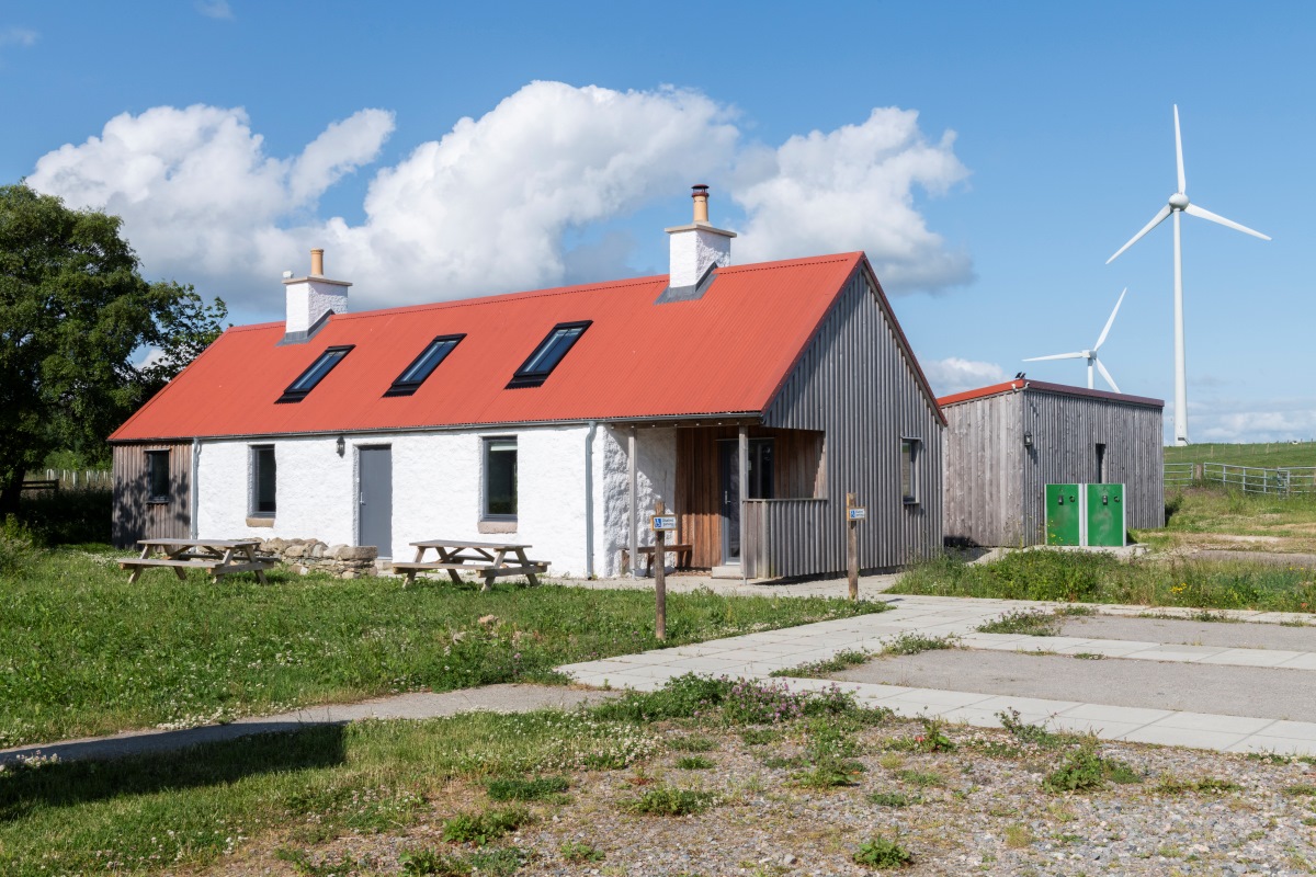 Farmhouse with wooden panels on the side, shed in the background and benches in front