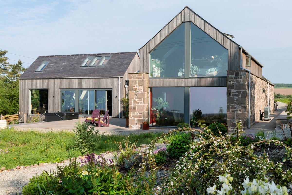 Large house with sandstone walls, large windows and wildflowers in the foreground