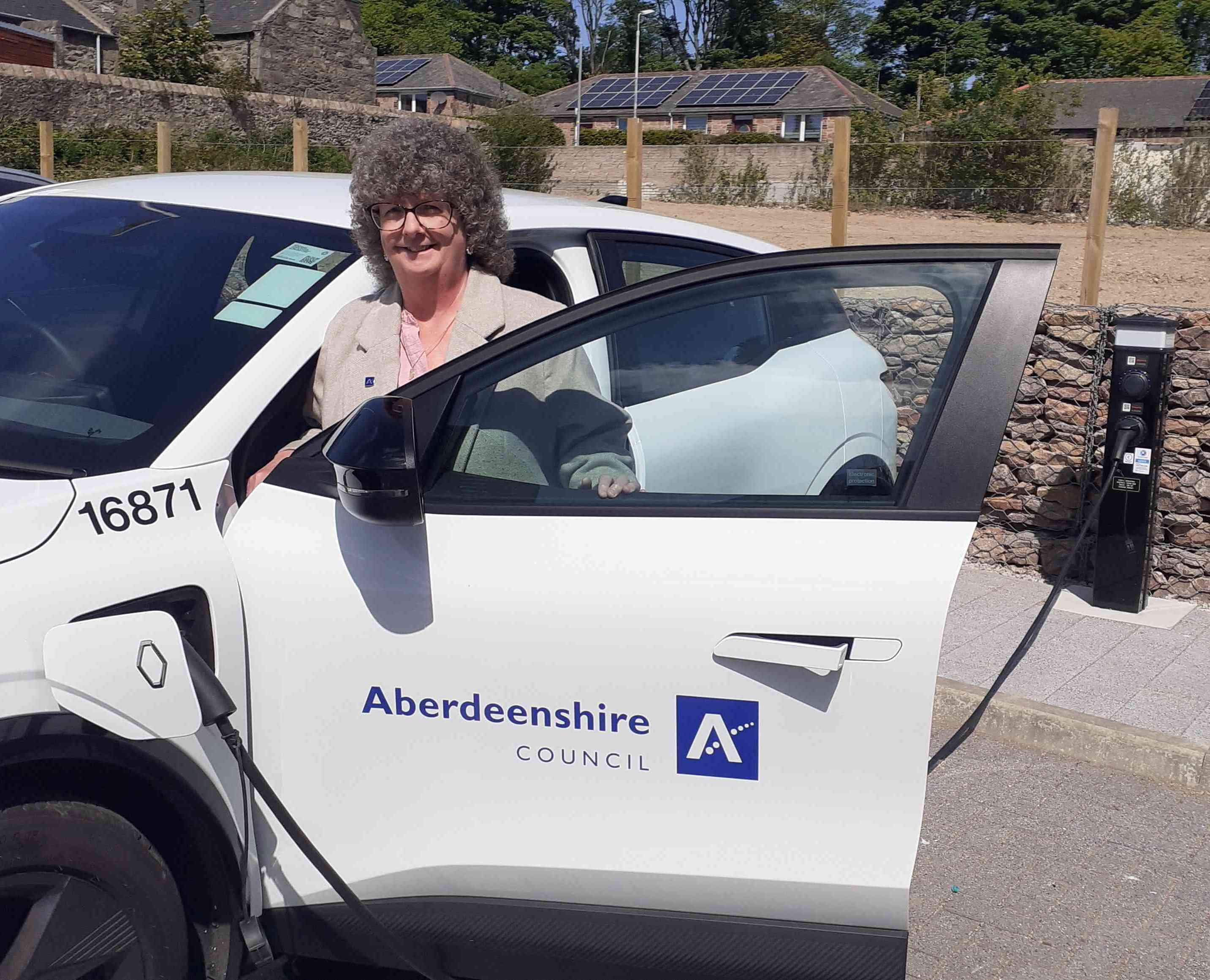 Leader of Aberdeenshire Council Councillor Gillian Owen standing at a white electric vehicle which is plugged into a charging unit