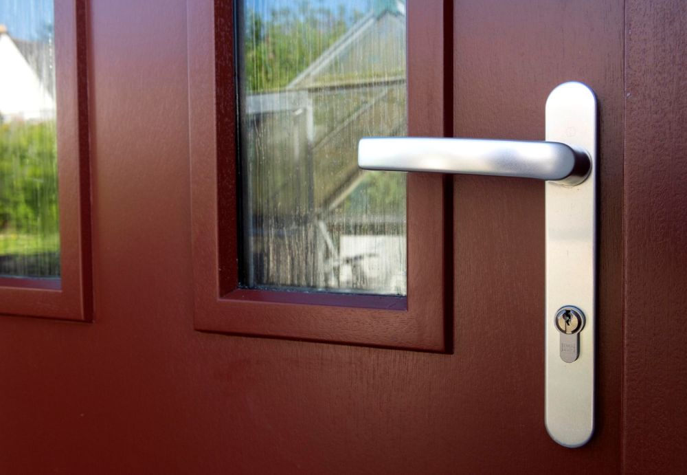 A close up of a red front door, showing two clear textured glass panels and a chrome door handle with a keyhole. 