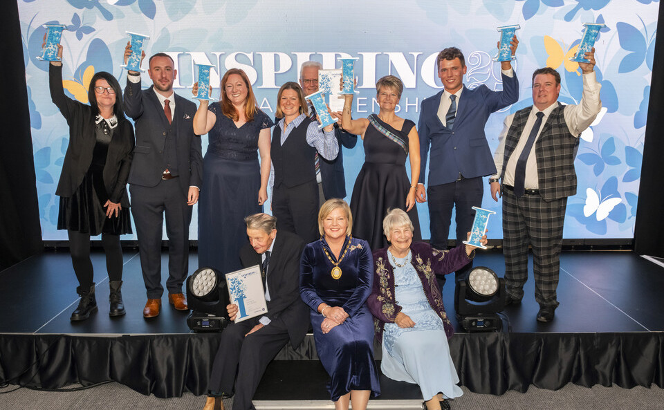 A group of people, some standing and some sitting, on a stage holding their awards
