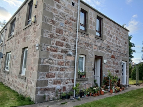 Block of flats with grass area, open front door and plant pots