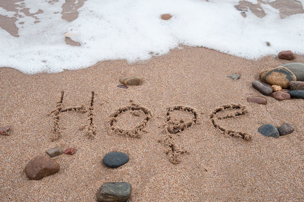 The word hope written in the sand by the sea.