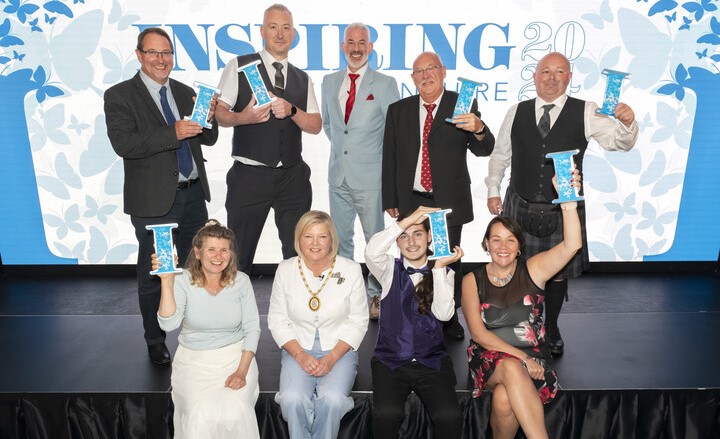 A group of people, some standing and some sitting, on a stage holding their awards