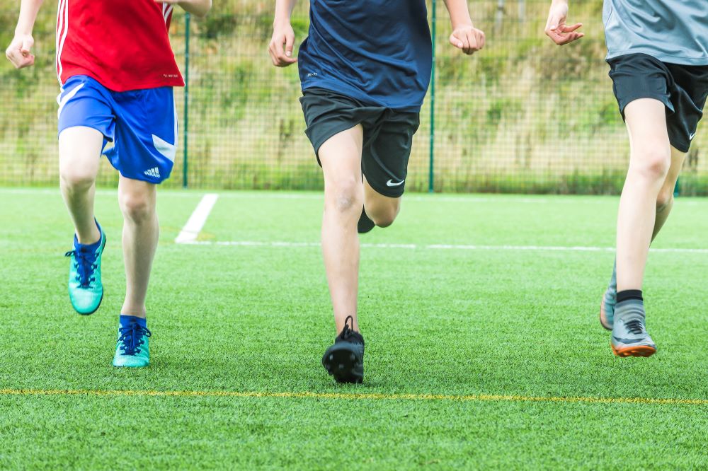 Three boys in short running in an enclosed green space. 