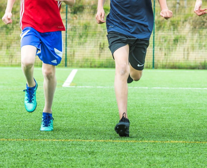 Three boys in short running in an enclosed green space. 