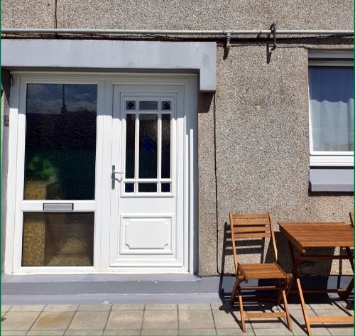 Front of house showing a glazed white door and window with a patio and outdoor seating